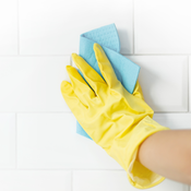 Hand wearing yellow rubber glove scrubbing tile grout